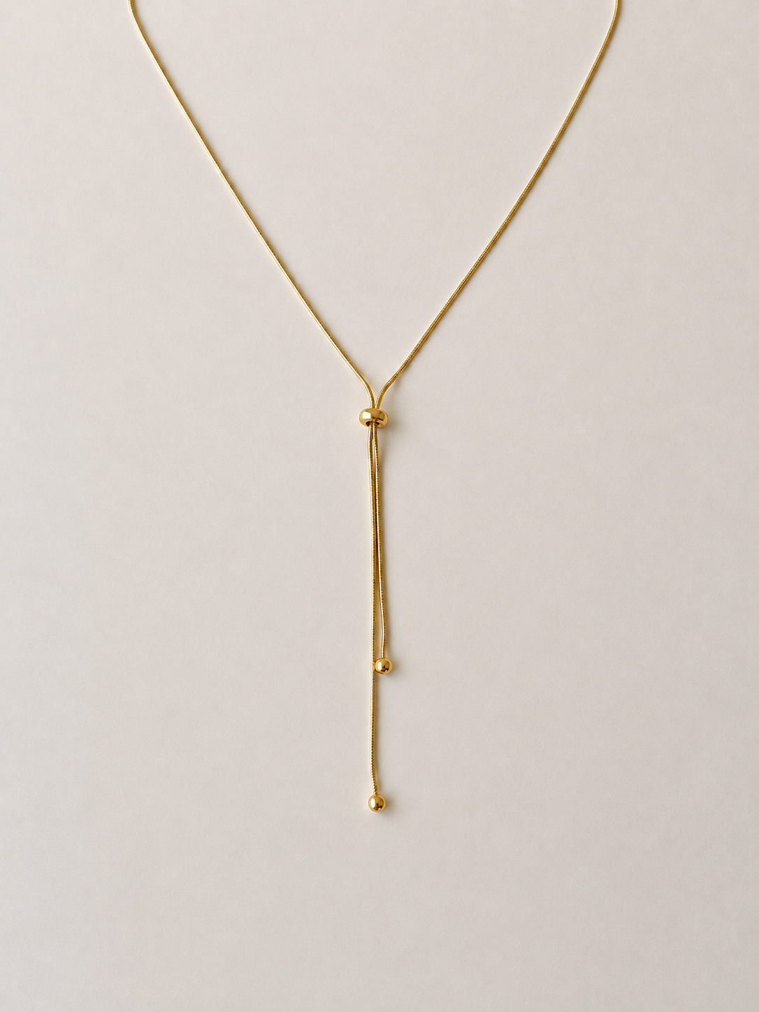 Adjustable snake chain lariat in 18K gold-plated S925 silver. Sliding bead adjuster, dual bead-tipped drops.