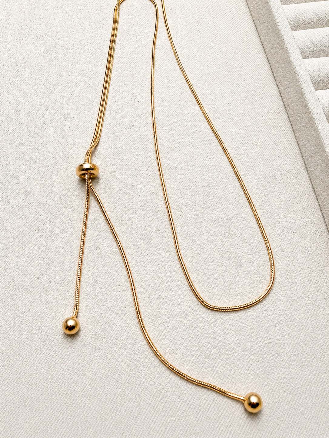 Adjustable snake chain lariat in 18K gold-plated S925 silver. Sliding bead adjuster, dual bead-tipped drops.